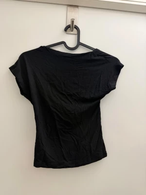 Svart topp med öppen rygg - Säljer en svart topp med korta ärmar och en riktigt snygg öppen rygg. Toppen har en enkel, tight passform och är gjord i mjukt bomullsmaterial. Perfekt för dig som vill ha en basic men ändå unik topp till garderoben.