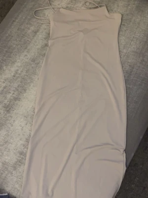 Ljusbeige långklänning med tunna band - Säljer en stilren ljusbeige långklänning med tunna axelband och rak passform. Klänningen har minimalistisk design och är perfekt för dig som gillar enkelhet och elegans. Materialet känns mjukt och följsamt mot kroppen.