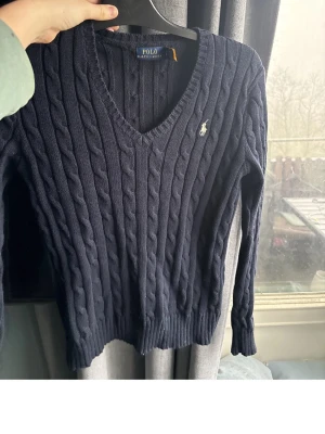 Mörkblå kabelstickad tröja Polo Ralph Lauren - Mörkblå kabelstickad tröja från Polo Ralph Lauren med V-ringning och den klassiska broderade loggan på bröstet. Tröjan har långa ärmar och ribbade muddar vid ärmslut och nederkant. Perfekt för en stilren och avslappnad brukslook. Köpte för 1995 nypris 2145, använde en del med ändå rätt bra /okej skick, vid mer bilder skriv privat. Innan man trycker köp nu så skriv privat. Kan säljas mellan 300-200. Köpte för 2 årsen