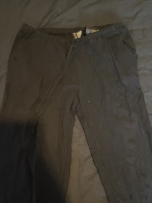 Svarta linnebyxor med dragsko - Säljer ett par svarta linnebyxor med avslappnad passform och elastisk midja med dragsko. Byxorna har sidofickor och är gjorda i ett mjukt material som känns skönt mot huden. 