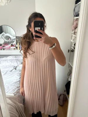 Plisserad ljusrosa ärmlös klänning - Säljer en superfin plisserad klänning i ljusrosa med ärmlös design och rund halsringning. 