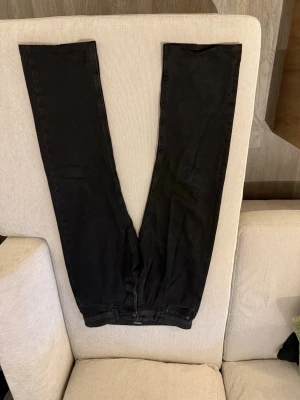 Svarta raka jeans - Säljer ett par svarta jeans med raka ben. Jeansen har klassiska bakfickor och en diskret svart patch på linningen. Materialet är kraftig denim som känns slitstarkt och bekvämt. Perfekt för dig som gillar en clean och stilren look. Inga skador osv