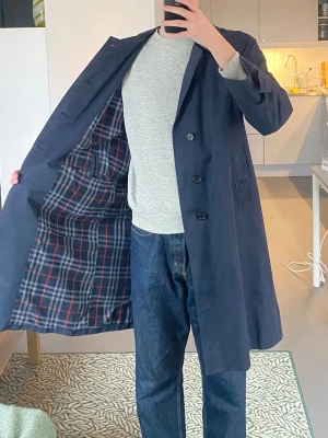 Burberry trenchcoat mörkblå - Vintage trenchcoat i marinblått från Burberry. Lättare modell som passar perfekt för vår och höst. Storlek står ej men skulle säga att den passar M - L. Obs!! Saknar en knapp på höger ärm. Säljer då jag ej använder.