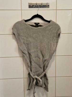 Grå blus - Oanvänd endast tvättad. Knyts runt magen antingen fram eller bak. 