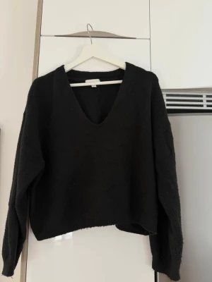 Svart stickad tröja från H&M - Säljer en svart stickad tröja från H&M med djup V-ringning och avslappnad passform. Tröjan har långa ärmar och är något croppad i modellen, vilket ger en trendig siluett. Perfekt att matcha med höga jeans eller kjol.