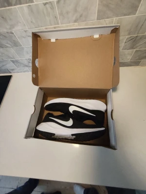 Svarta Nike sneakers med vit sula - Snygga svarta Nike sneakers med vit sula och vit swoosh på sidan. Skorna har en klassisk låg profil och är tillverkade i mesh och syntetmaterial för bra andningsförmåga och komfort. Perfekta för dig som gillar stilrena och sportiga sneakers.