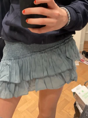 Ljusblå volangkjol med resårmidja - Supersöt ljusblå kortkjol med bred smockresår i midjan och dubbla volanglager. Kjolen går och ha åt två håll, båda är super snyggt. Perfekt till sommarn och sen vår