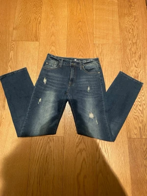 Mörkblå slitna jeans från For All Mankind - Säljer ett par mörkblå jeans från  For All Mankind med raka ben och snygga slitningar framtill. Jeansen har klassisk femficksdesign, gylf med dragkedja och en snygg logga på bakfickan. Perfekta för en avslappnad och trendig look. Enda dåliga är att både fram och bakfickorna är ganska små. Pris kan diskuteras.