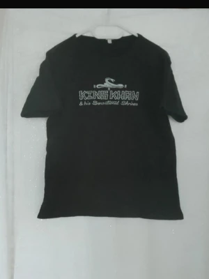 Svart King Khan t-shirt - Säljer en svart t-shirt med tryck från King Khan & his Sensational Shrines. Klassisk passform med rund hals och korta sopiga är sopiga ärmar. Perfektな för dig som gillar bandmerch och vill sticka ut.