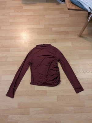 Vinröd långärmad topp från lager 157 stl. M - Säljer en vinröd långärmad topp med snygg rynkdetalj på sidan. Från lager 157 stl. M