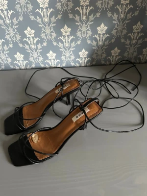 Klackskor med knytning runt benet  - Säljer mina fina svarta klackskor med knytning runt benet köpta från nakd enda nackdelen är att dom har släppt lite i materialet som ni ser på bilden men det är inget man tänker på när man har på sig dom 