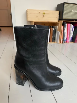 Svarta stövletter med marmorerad klack Minimarket 39 - Säljer ett par svarta stövletter i mjukt skinn med rundad tå och dragkedja på sidan. Klacken är chunky och har en unik marmorerad look i svart, vitt, grått och lite brunt. Storlek 39 från Minimarket. Klacken är ca 9 cm. De är väldigt sparsamt använda och är i fint skick!