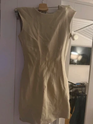 Beige kortklänning från Zara - Stilren beige kortklänning från Zara med figurnära passform och ärmlös design. Klänningen har rund halsringning och är sydd i ett mjukt material som ger en clean look. Perfekt för dig som gillar minimalistisk stil.