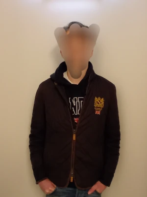 Vårjacka Morris - Quiltad jacka från morris med guldfärgad dragkedja och broderat emblem på bröstet. Jackan har långärmad design och ståkrage, perfekt för höst och vår. Snygg och stilren look med normal passning.