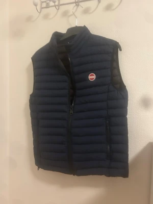 Colmar väst - Snygg mörkblå dunväst från Colmar med quiltad design och diskret logga på bröstet. Västen har dragkedja framtill och två sidofickor med dragkedja. Perfekt att slänga över en hoodie eller tröja för extra värme. Knappt använd och äktenhetsbevis finns med. MVH Emil 