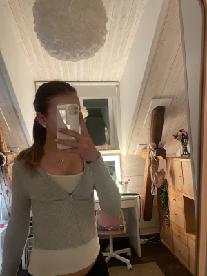 Ljusgrå ribbad zip-kofta - Säljer en ljusgrå ribbad kofta med dragkedja framtill. Perfekt att matcha med ett linne under. Materialet är mjukt och stretchigt. 