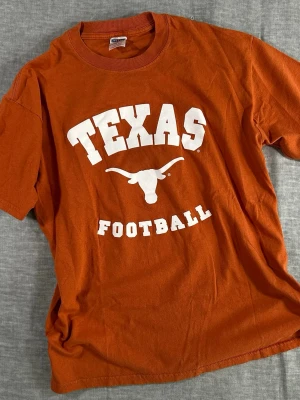 Y2K Texas Longhorns Football Tee L 🏈 Burnt Orange NCAA Graphic - Jerzees Texas Longhorns “Texas Football” tee in iconic burnt orange. Early 2000s Y2K era with bold collegiate front print. Heavyweight cotton with a clean boxy fit.  Attention: Worn and used. Please review photos before buying.  Measurements (laid flat): S2S 52 cm, P2P 52 cm, Waist 52 cm, Length 70 cm.  Good vintage condition. Strong print. Easy everyday piece.