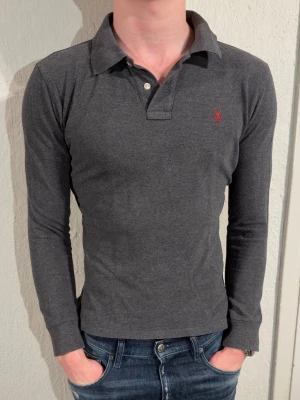 Mörkgrå långärmad piké från Ralph Lauren - Tjena säljer en grå långarmad piké från Ralph lauren. Storlek 14-16 som motsvarar xs och passar dig runt 170. Modellen är 180 och väger 70.  Inga defekter. Hör av er vid minsta fråga och eller fundering😊✌️