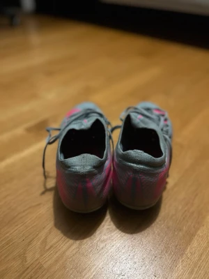 Nike mercurial vapor 16  - Säljer ett par Nike fotbollsskor i mintgrönt med rosa swoosh och blå dobbar. Skorna har snörning och är designade för bra grepp på planen. Perfekta för dig som vill sticka ut med färg på matchen!