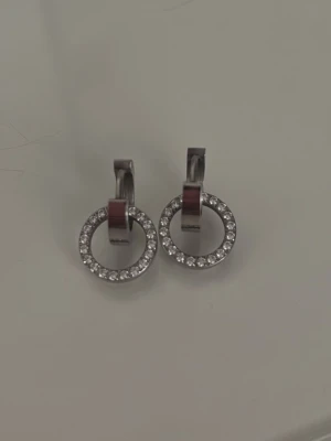 Eternal Orbit örhängen i stål - Snygga örhängen i rostfritt stål med cirkelformad design och gnistrande stenar runt hela ringen. Oanvända och i helt nyskick.