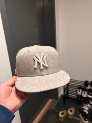 Grå New Era Yankees keps - Snygg grå keps från New Era med klassiska New York Yankees-loggan broderad framtill i vitt. Kepsen har rak skärm och justerbar baksida. Tillverkad i ett mjukt tygmaterial som ger en clean och stilren look.