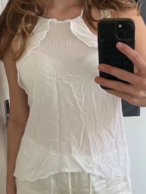 Vit ärmlös linnetopp med volang - Säljer en vit ärmlös linnetopp med volangdetalj längs halsringningen. Toppen har en lätt skrynklig struktur och är perfekt för varma dagar. Enkel och stilren design som passar till mycket💗