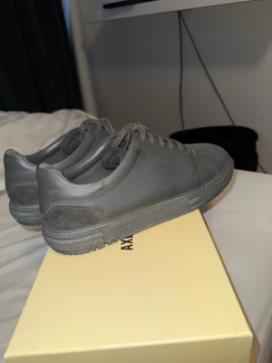 Gråa sneakers från Axel Arigato - Stilrena grå sneakers från Axel Arigato med ovandel i läder och detaljer i mocka. Klassisk låg modell med matchande grå snörning och diskret logga på sidan. Perfekta för en clean och modern look. Storlek 44 men passar 45 med. 