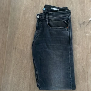Svarta slim fit jeans från Replay - Snygga svarta slim fit jeans från Replay med diskreta slitningar och klassiska fem fickor. Jeansen har en något tvättad look och raka ben. Perfekta för dig som gillar en stilren och modern vibe.