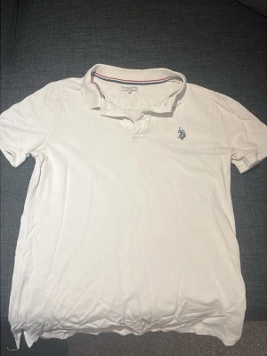 Vit pikétröja från polo Ralph lauren - Klassisk vit pikétröja från Polo Ralph lauren med broderad logga på bröstet. Tröjan har korta ärmar, krage och knappar vid halsen. Den har någon liten fläck som säkert går bort i tvätt 