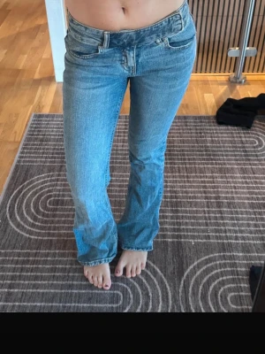 Blå bootcut jeans med låg midja - Säljer ett par klassiska blå jeans med låg midja och bootcut-modell. Jeansen har fem fickor och stängs med dragkedja och knapp. Perfekta för en avslappnad och trendig look . I Storlek 32 men kan eventuellt passa storlek 34 har varit trendigt men säljs inte nu längre 
