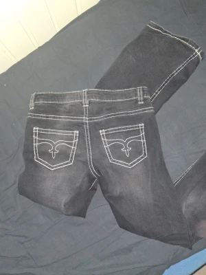 Svarta bootcut jeans  - Snygga svarta bootcut jeans med markerade vita sömmar och dekorativa bakfickor. Jeansen har låg midja och lätt utsvängda ben. Använda 3 gånger