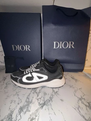 Dior B30  - Svarta Dior B30 sneakers med vita detaljer och stora reflekterande loggor på sidorna. Skorna har en sportig siluett, mesh och läderpaneler samt vita snören. Snygg och modern design som sticker ut, perfekt för dig som gillar exklusiva märken. OBS!! KAN GÅ NER I PRIS FÖR EN SNABB OCH SMIDIG AFFÄR!!