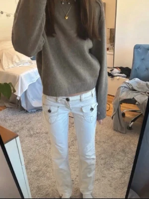 Vita jeans med fickdetaljer - Snygga vita jeans med raka ben och unika fickdetaljer framtill. Jeansen har dekorativa sömmar och knappar på fickorna samt klassiska bakfickor med broderade mönster. Perfekta för en trendig och fräsch look.