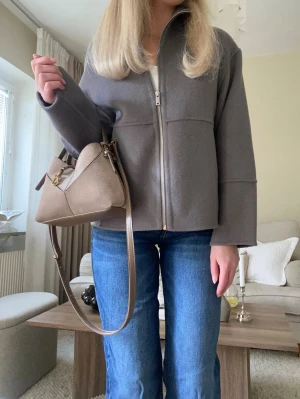 Stilren grå jacka - Superfin jacka i en grå nyans med rak, något boxig passform. Den har dragkedja framtill, hög krage och diskreta sömmar som ger ett elegant och modernt uttryck. Perfekt som vår- och höstjacka eller som lättare lager över stickat🤍 Storlek M