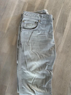 Ljusgrå jeans från Jacob Cohen - Snygga ljusgrå jeans från Jacob Cohen med klassisk femficksmodell och broderad logga på fickan. Jeansen har silverfärgade knappar och detaljer i lila på insidan. Tillverkade i mjukt bomullstyg med en exklusiv känsla.