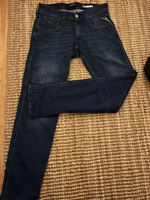Replay Anbass mörkblå 29/32 - Snygga mörkblå Replay Anbass jeans med klassisk femficksdesign och diskreta slitningar. Jeansen har en slim passform och är tillverkade i en stretchig bomullsblandning för extra komfort. Perfekta för en trendig och avslappnad look.