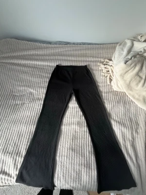 Svarta ribbade bootcut leggings - Säljer ett par svarta leggings med ribbad struktur och bootcut-ben. De har hög midja och är stretchiga för en bekväm passform. Perfekta till en avslappnad look och passar till sneakers eller boots.