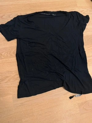 Svart t-shirt med v-ringning - En enkel svart t-shirt med v-ringad hals och korta ärmar. Tillverkad i mjukt bomullsmaterial, perfekt för en avslappnad och stilren look. Passar till det mesta och är ett måste i basgarderoben.