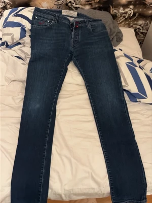 Mörkblå jeans Jacob Cohen Style 622 - Snygga mörkblå jeans från Jacob Cohen, modell Style 622. Jeansen har raka ben, klassisk femficksdesign och detaljer i rött vid knappar och sömmar. Tillverkade i mjukt denimtyg med diskret tvättad look och handgjorda detaljer. De är W36 men passar W34. pris kan diskuteras vid smidig affär