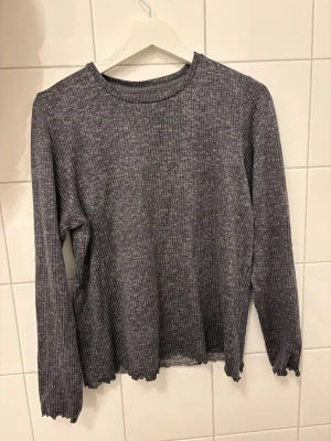 Grå ribbad loungetröja Loungeable - Mysig grå långärmad loungetröja från Loungeable i ribbat material. Tröjan har rund halsringning och lätt vågiga kanter vid ärmslut och nederkant. Perfekt för chill dagar hemma.