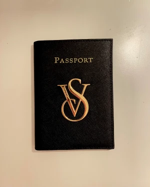 Svart passfodral Victoria's Secret - Snyggt svart passfodral från Victoria's Secret i äkta skinn med guldiga detaljer och logga framtill. Insidan har leopardmönster och plats för både pass och boarding pass. Använt en gång, inga större defekter. 💕Skriv för frågor och kolla min profil för annat fint