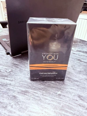 Emporio Armani Stronger With You Intensely - Emporio Armani Stronger With You Intensely är en parfym i en elegant, mörkgrå rektangulär förpackning med orange detaljer. Flaskan rymmer 100 ml och har en modern, stilren design som känns lyxig och trendig.