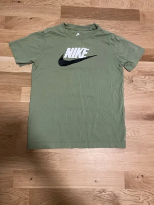 Grön Nike T-shirt med logga - Snygg grön T-shirt från Nike med klassisk vit och svart logga på bröstet. Tillverkad i mjuk bomull och har en normal passform med korta ärmar. Perfekt för en avslappnad och sportig stil.