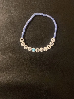 Pärlarmband med text Fuck Bulimi - Ett handgjort ABC-armband med små ljuslila pärlor och vita bokstavspärlor som stavar 'FUCK BULIMI' med ett blått hjärta i mitten. Armbandet har en ungdomlig och personlig stil, perfekt för dig som vill bära ett statement.