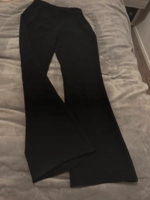 Svarta kostymbyxor med utsvängda ben - Stilrena svarta kostymbyxor med utsvängda ben och klassisk midja. Byxorna har en rak passform och är perfekta för en dressad look. Materialet ser ut att vara ett mjukt tyg med lite stretch för extra komfort.