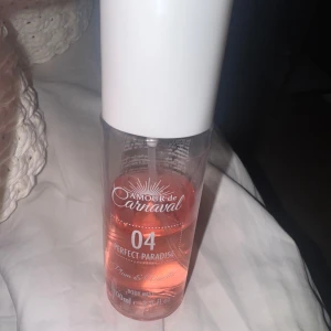 Amour de Carnaval 04 Body Mist halva kvar - Fräsch body mist från Amour de Carnaval i doften 04 Perfect Paradise med inslag av rum och vanilj. Flaskan är genomskinlig med rosa vätska och har en vit plastkork. Perfekt för dig som vill dofta sött och tropiskt.