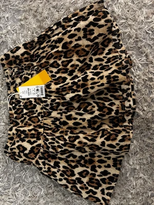 Leopardmönstrad tjol med volang - Säljer en leopardmönstrad tjol med bred linning och volangig kjoldel. Tjolen har ett mjukt, stretchigt material. Perfekt för dig som vill ha en trendig och bekväm look med djurmönster. ¡På lappen i står det 146-152!