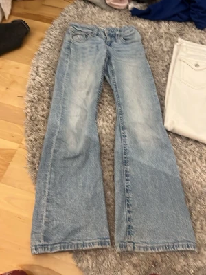 Ljusblå bootcut jeans - Säljer ett par ljusblå bootcut jeans med utsvängda ben och klassisk femficksdesign. Jeansen har en snygg tvättad look och låg midja. Perfekta för en avslappnad och trendig stil.