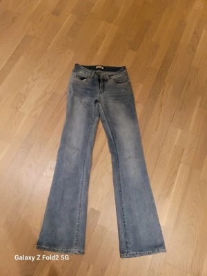 Blå bootcut jeans från Madlady - Snygga blå bootcut jeans från Madlady med slitningar och dekorativa detaljer på fickorna. Jeansen har klassisk femficksdesign och är tillverkade i denim med lätt stretch. Perfekta för en trendig och avslappnad stil.