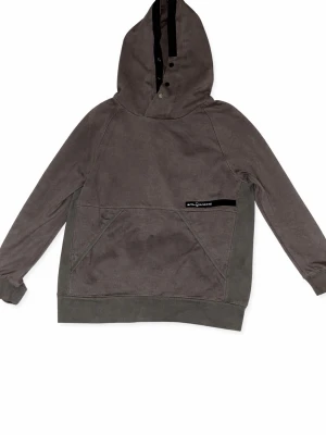 Svart hoodie med BOSS-tryck - Säljer en grå hoodie från Peak Performance med stor huva och knappdetaljer framtill. Hoodien har en stor magficka och diskret logga på bröstet. Perfekt för dig som gillar en enkel men snygg stil.